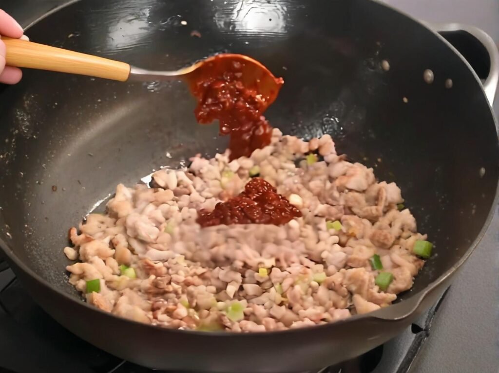 Add minced garlic, ginger, and scallions, then stir-fry for 30 seconds.
Stir in the doubanjiang and cook until the oil turns red and fragrant.